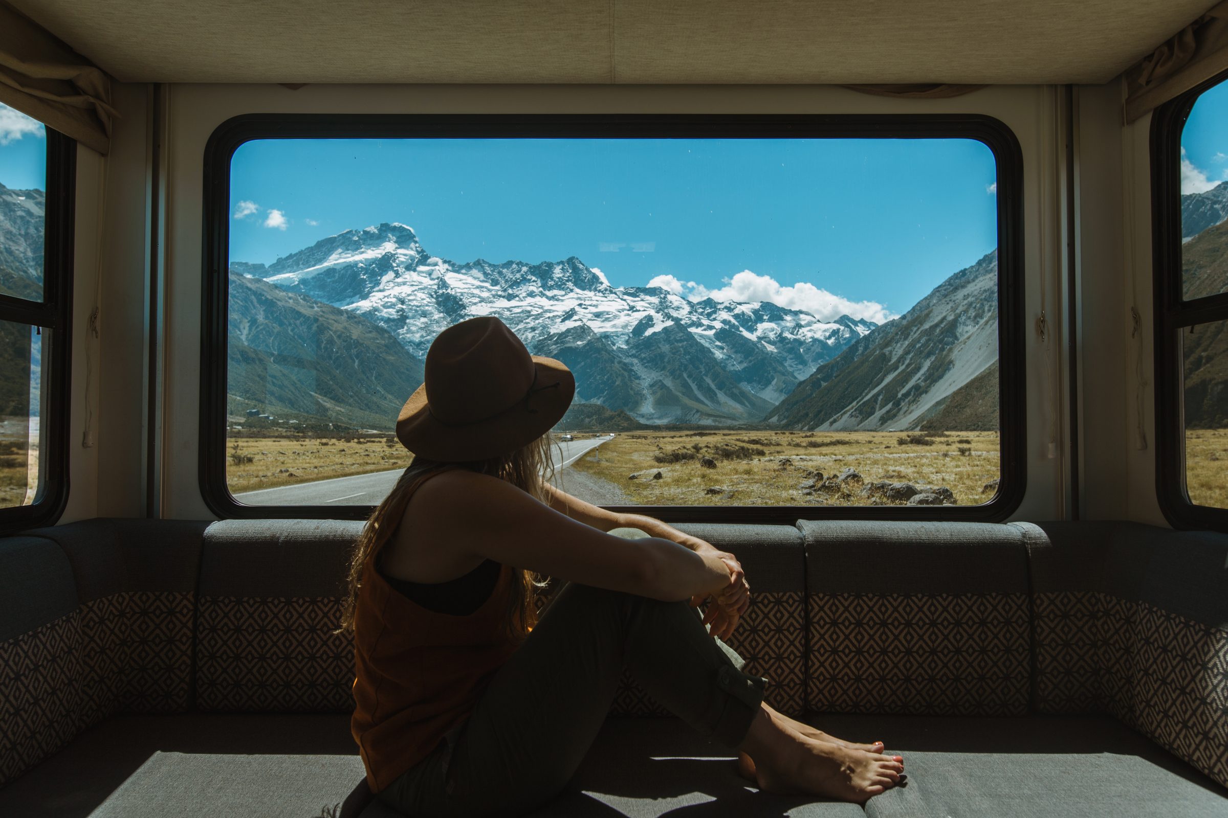 A traveler in a hat looks through a window at snowy mountains
